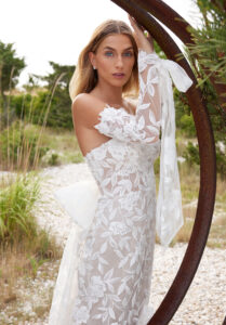 Santana wedding dress by Morilee, a strapless fit and flare gown with bold floral beaded lace, detachable bow, and sheer long sleeves with bow cuffs
